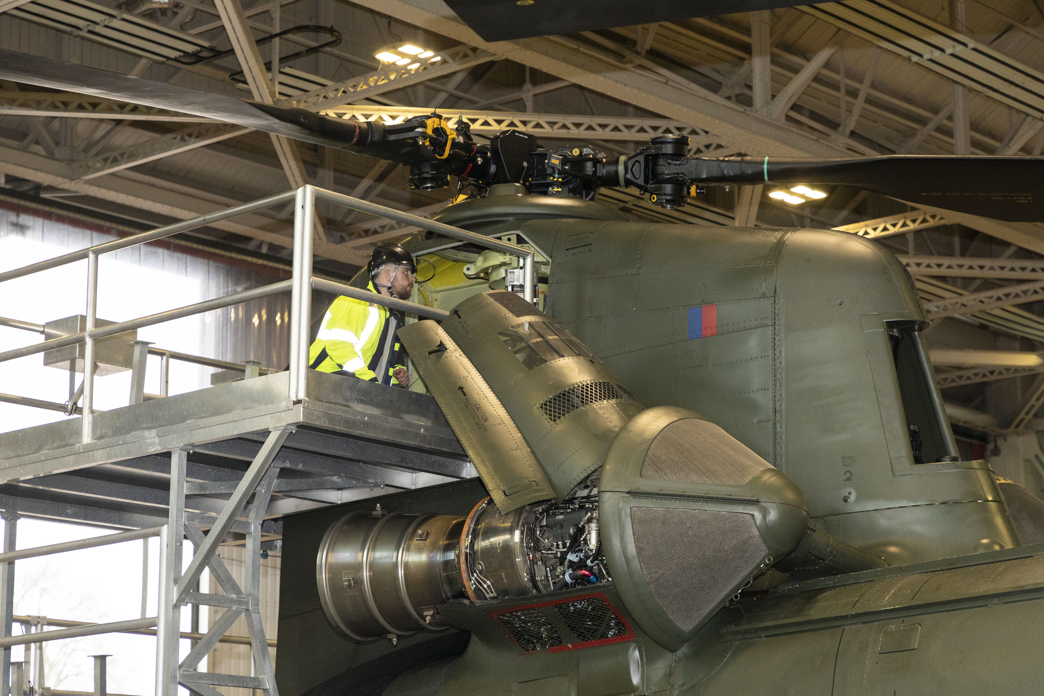 Image shows aviator checking helicopter parts in hangar.